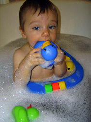 Kenji bites his rubber ducky in the bubble bath.